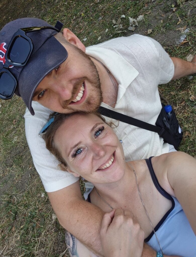 Zomerse foto's van een blij stel dat samen op de grond ligt, genietend van de buitenlucht, met een natuurlijke omgeving en grassprietjes om hen heen.