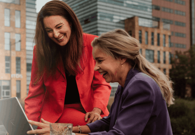Twee collega's zitten buiten te overleggen achter een laptop.