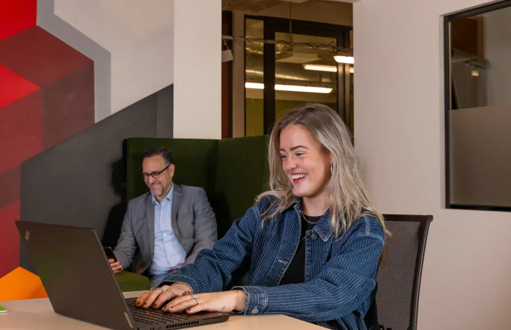 een collega lachend aan het werk achter een bureau.