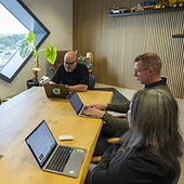 Collega's zitten aan een tafel in een vergaderkamer op kantoor en kijken op hun laptop.