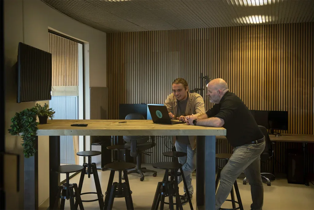 Twee collega's staan aan een tafel en kijken naar een laptop.