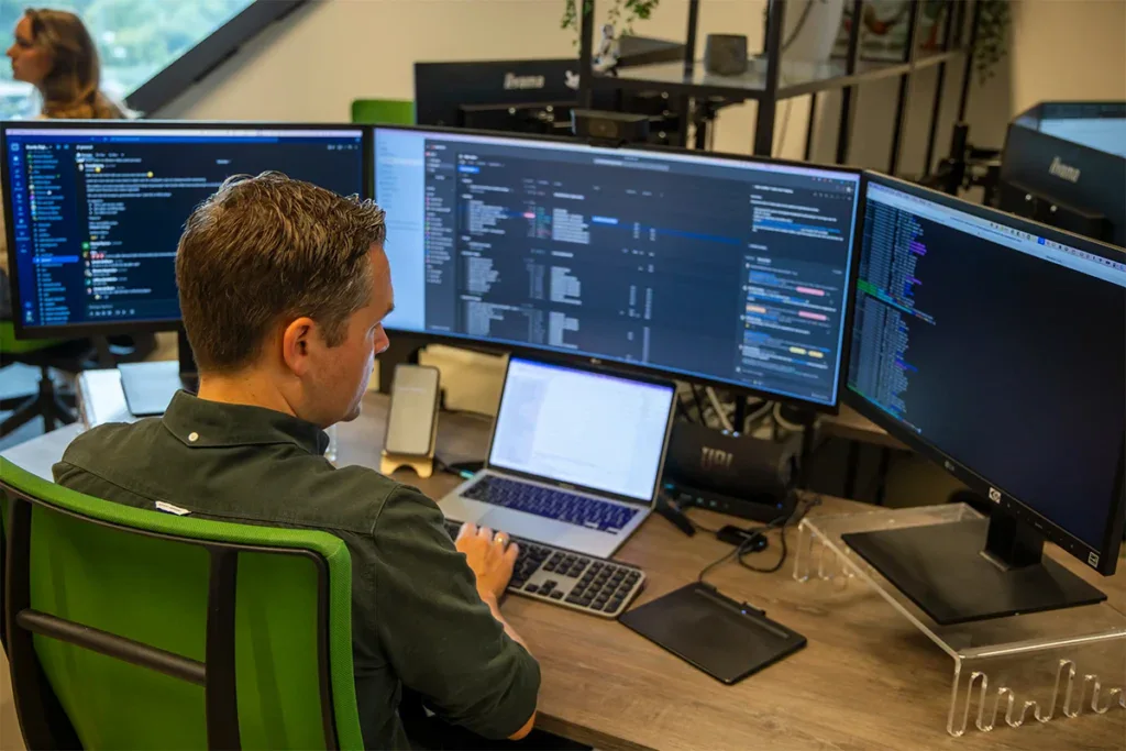 Back end developer zit achter zijn bureau op kantoor en is aan het programmeren.