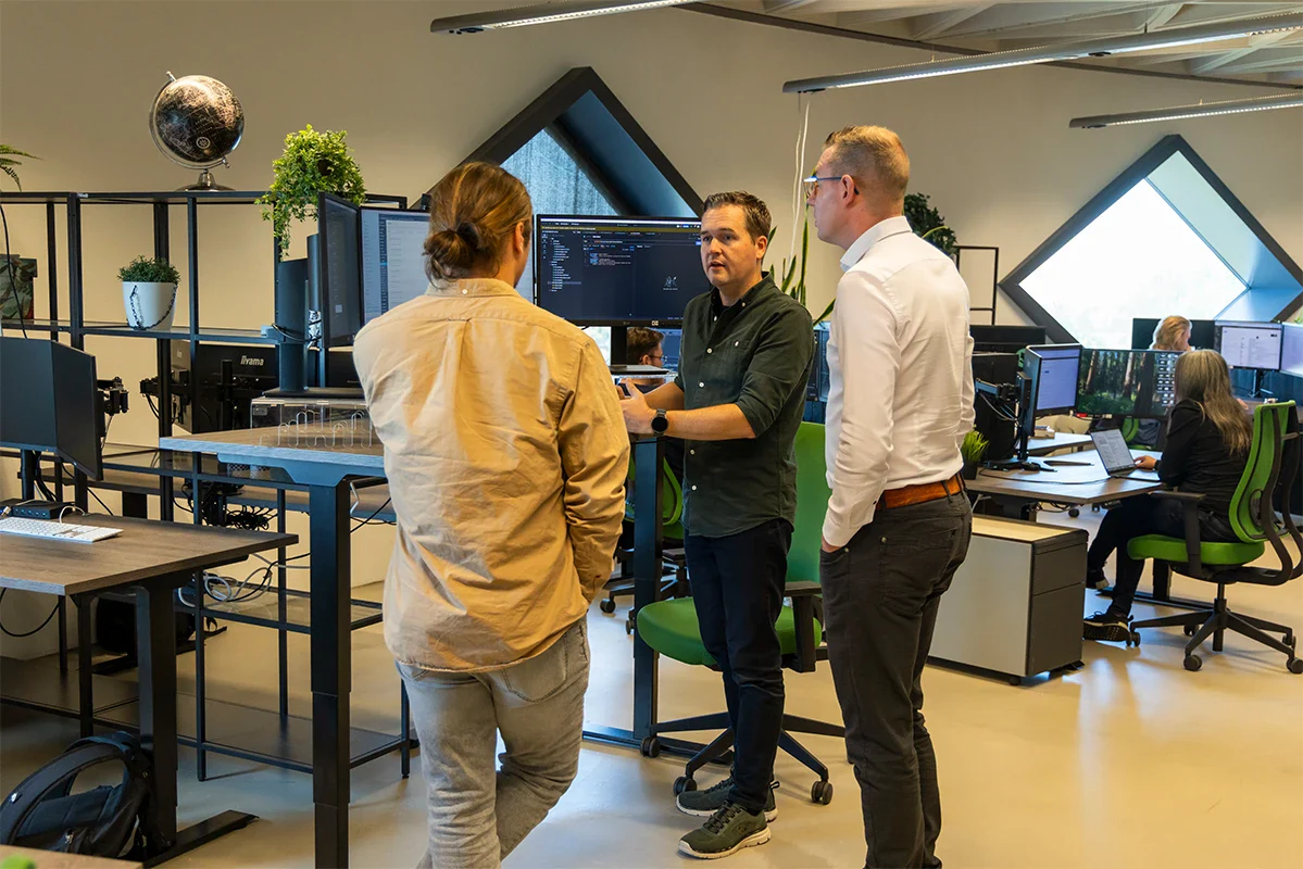 Drie developers staan bij een bureau en overleggen op kantoor.