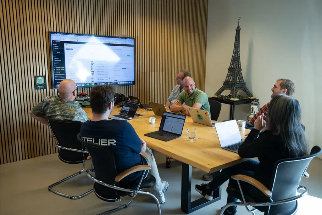 Development team zit aan een grote tafel en overlegd in een vergaderruimte.