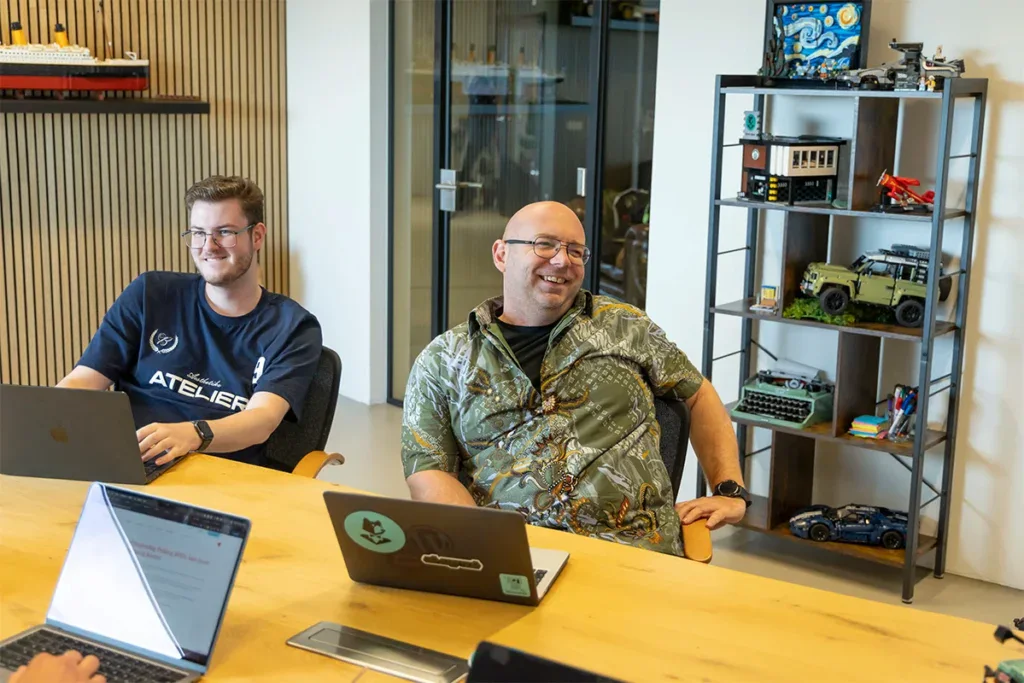 Twee programmeurs zitten aan tafel tijdens een meeting in een vergaderruimte.