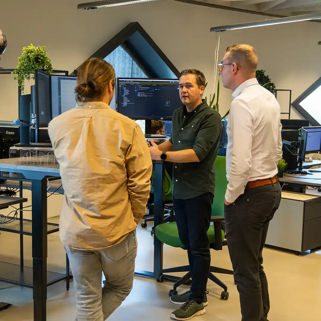 Collega's zijn staand aan het overleggen bij Michael zijn bureau op kantoor bij een laptop.