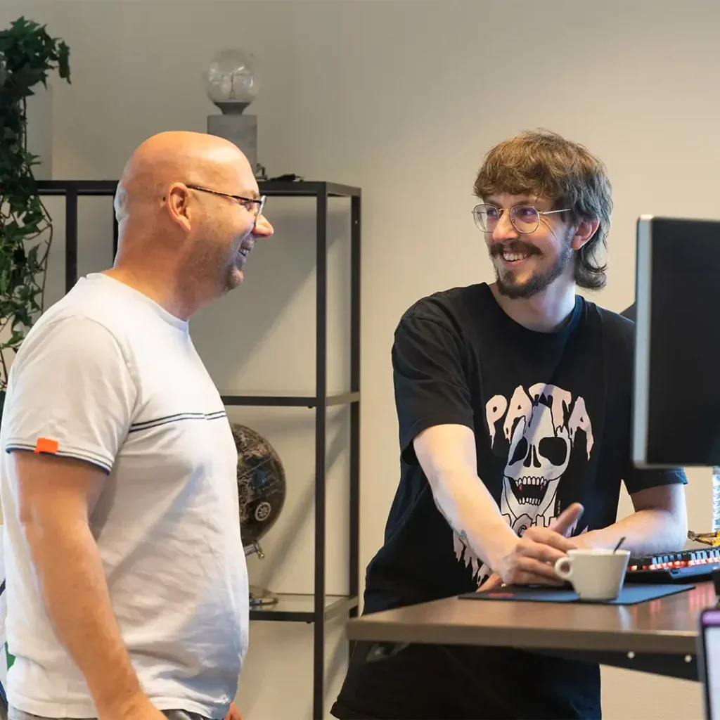 Programmeur zijn aan het overleggen achter hun bureau en lachen daarbij.