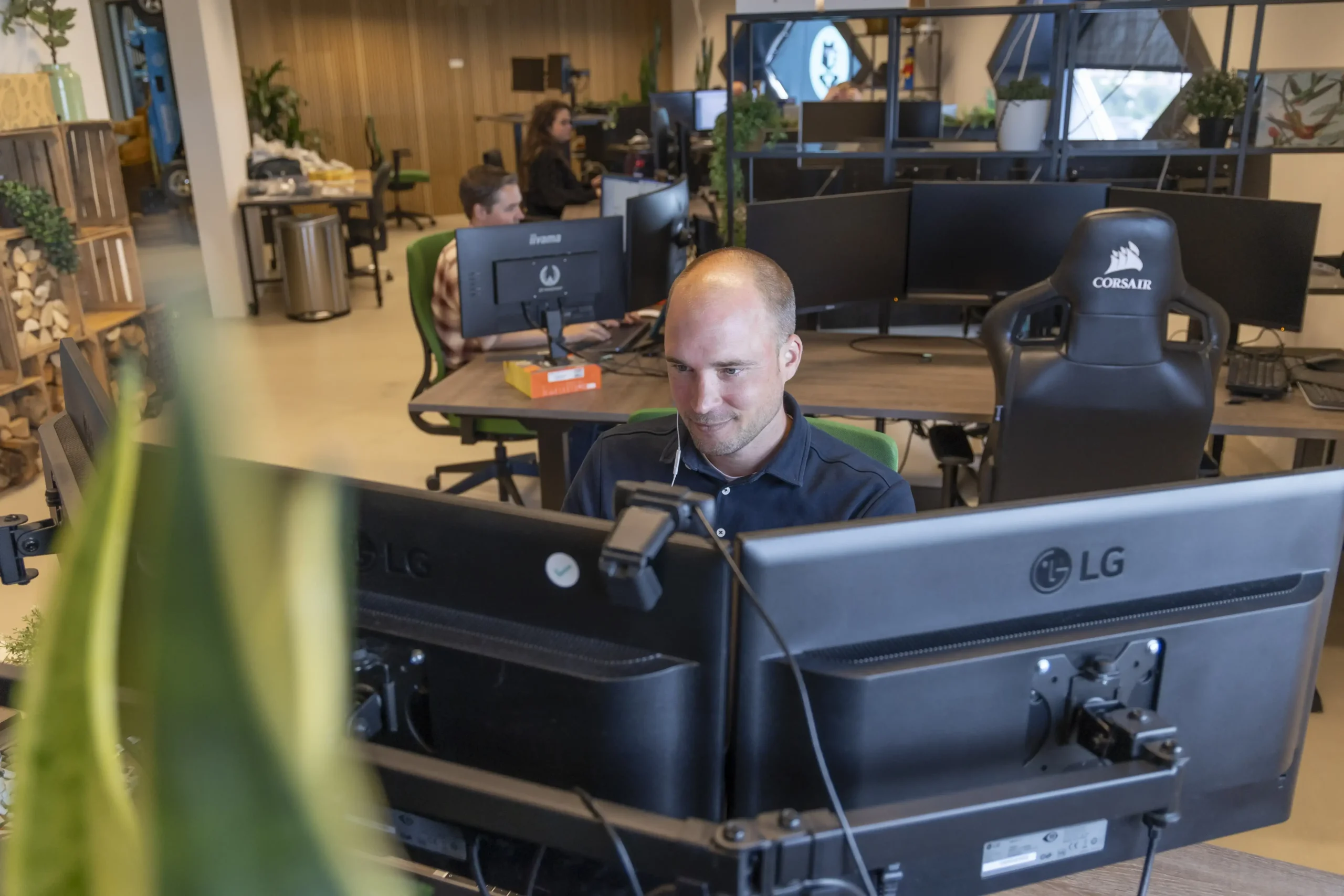 Front end developer zit achter zijn bureau te programmeren, op de achtergrond zie je collega's aan het werk.