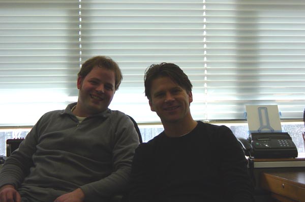 Mensen zitten in kantoor met daglicht en blinden, bedrijfslogo op achtergrond.